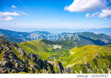 A hiker journeys through the lush green valleys of Low Tatras National Park in Slovakia, surrounded by stunning mountain scenery and clear blue skies on a bright sunny day. A hiker journeys through the lush green valleys of Low Tatras National Park in Slovakia, surrounded by stunning mountain scenery and clear blue skies on a bright sunny day. 124147017