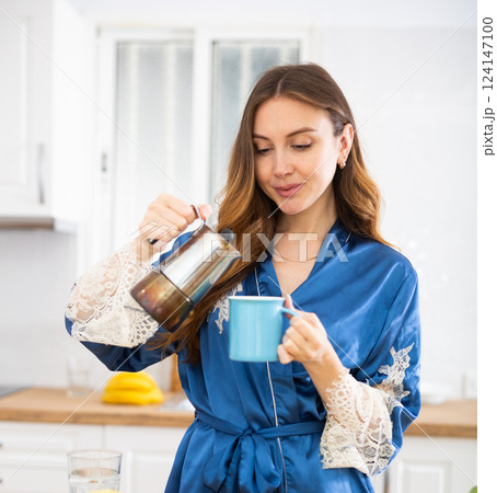 Woman in housecoat making coffee in kitchen Woman in housecoat making coffee in kitchen 124147100