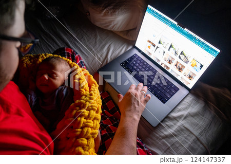 Father Holding Baby While Using Laptop in Dim Light Father Holding Baby While Using Laptop in Dim Light 124147337