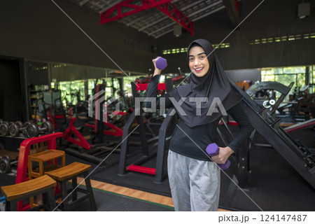 Arab middle eastern muslim woman working out while lifting a dumbbell at the gym. Fitness exercise and healthy lifestyle concept 124147487