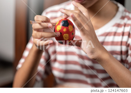 Indonesian southeast asian little girl is painting on an egg with a paintbrush for easter egg decoration on the table. Concept of celebrating the easter holiday Indonesian southeast asian little girl is painting on an egg with a paintbrush for easter egg decoration on the table. Concept of celebrating the easter holiday 124147603