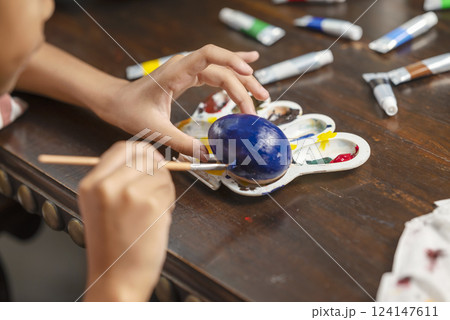 Indonesian southeast asian little girl is painting on an egg with a paintbrush for easter egg decoration on the table. Concept of celebrating the easter holiday 124147611