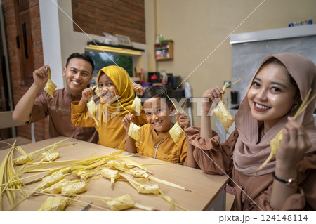 Indonesian Muslim family weaving ketupat rice dumpling from young coconut leaves. Traditional Muslim food during celebration of Happy Lebaran, Eid Al Fitr, Idul Fitri, and Ramadan Mubarak celebration 124148114