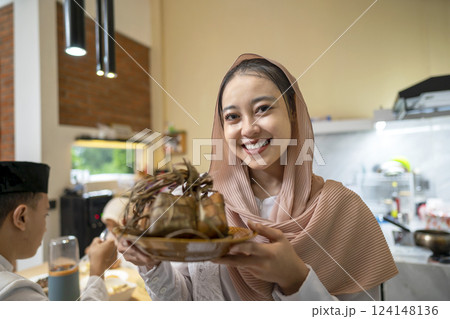 An Indonesian Muslim mother showing ketupat rice dumpling on the plate. Traditional Muslim food during the celebration of Happy Lebaran, Eid Al Fitr, Idul Fitri, and Ramadan Mubarak celebration 124148136