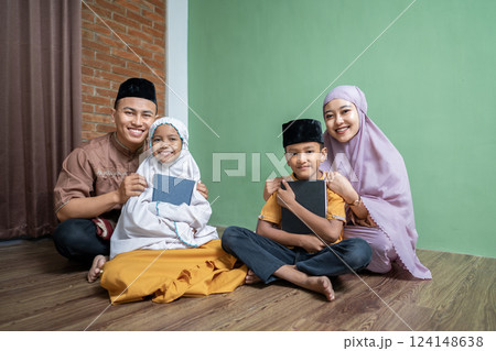 Portrait of an Indonesian Muslim family hugging their child while holding the quran. Concept of the Islamic holy book or Ramadan Kareem Portrait of an Indonesian Muslim family hugging their child while holding the quran. Concept of the Islamic holy book or Ramadan Kareem 124148638