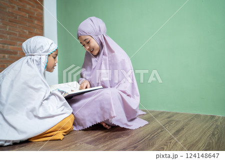 Portrait of an Indonesian Muslim mother teaching her daughter to read the quran. Concept of the Islamic holy book or Ramadan Kareem 124148647