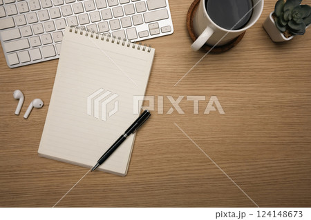 Minimalist workspace with notebook and coffee cup and wireless earbuds on wooden desk 124148673