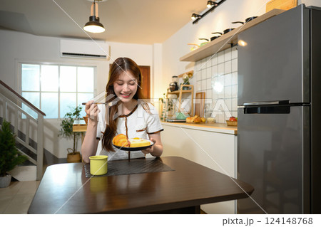 Beautiful young woman enjoying a delicious breakfast in a cozy home kitchen 124148768
