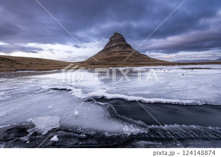 Flowing water from Kirkjufellsfoss waterfall with a view of Kirkjufell mountain on peninsula, Iceland 124148874