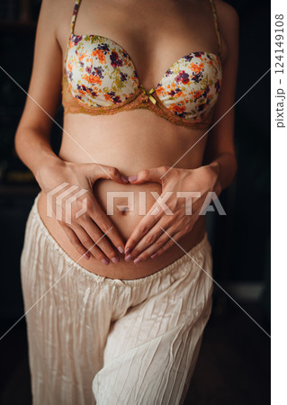 Pregnant young woman creating heart shape with hands on her belly 124149108