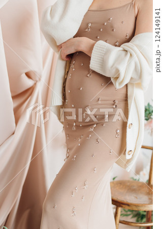 Pregnant young woman in elegant dress posing indoors with soft decor Pregnant young woman in elegant dress posing indoors with soft decor 124149141