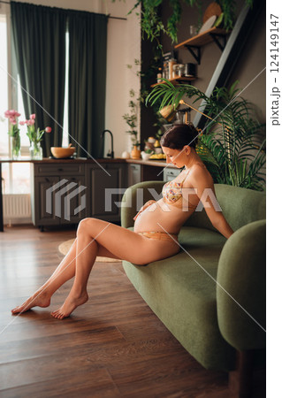 Pregnant young woman relaxing on a green couch in a cozy living room Pregnant young woman relaxing on a green couch in a cozy living room 124149147