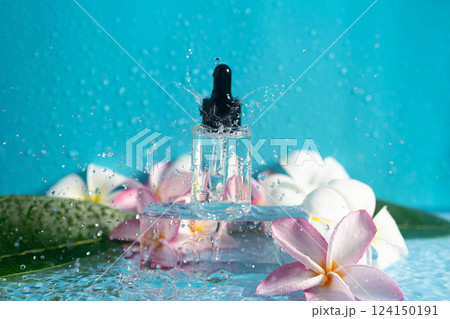 A dropper bottle of hydrating serum rests on a clear surface with plumeria flowers and water. A dropper bottle of hydrating serum rests on a clear surface with plumeria flowers and water. 124150191
