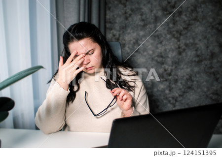 Tired woman working at home with laptop holding eyeglasses rubbing eyes and feeling fatigue. Stress and frustration concept. Tired eyes Tired woman working at home with laptop holding eyeglasses rubbing eyes and feeling fatigue. Stress and frustration concept. Tired eyes 124151395