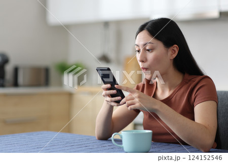 Surprised asian woman using smart phone in a kitchen 124152546