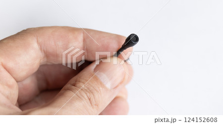 A close-up of a hand holding a small black wired microphone against a white background. The tiny microphone has a thin cable and a mesh-covered tip, designed for discreet audio recording. A close-up of a hand holding a small black wired microphone against a white background. The tiny microphone has a thin cable and a mesh-covered tip, designed for discreet audio recording. 124152608
