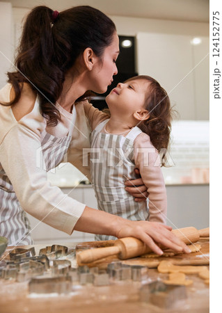 Happy mother and smiling cute little child daughter rolling dough for homemade pastry. Happy mother and smiling cute little child daughter rolling dough for homemade pastry. 124152775