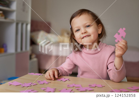 smiling little child girl showing puzzle piece at wooden desk in room 124152858