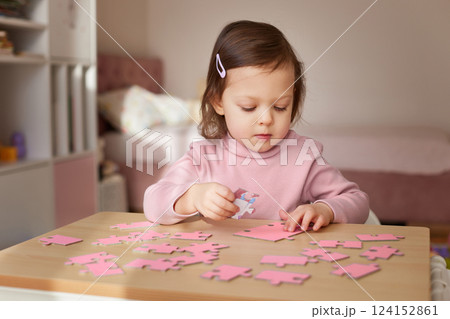 Cute little child girl connecting puzzle pieces on wooden desk in room Cute little child girl connecting puzzle pieces on wooden desk in room 124152861