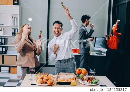 Asian office colleagues and friends enjoy a daytime BBQ with pizza and beer, celebrating Halloween and cheering for their favorite soccer team, creating a lively atmosphere filled with joy. 124153217