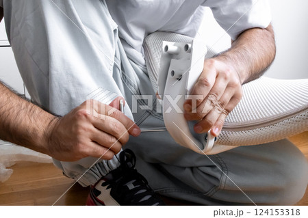 Adult male assembling office chair using hex key tool on wooden floor 124153318