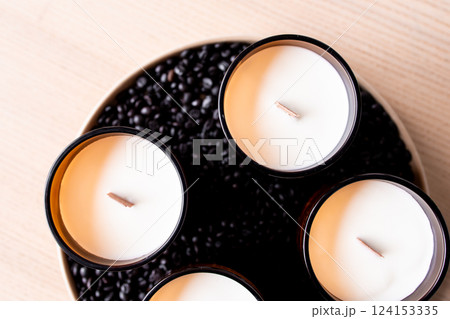 Top view of scented candles in glass holders surrounded by black beans on wooden surface 124153335