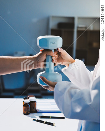 Asian caregiver woman or nurse training senior woman lifting dumbbell for arm exercise while therapy and rehabilitation in living room at home, caretaker or physiotherapist helping elderly workout. 124154642