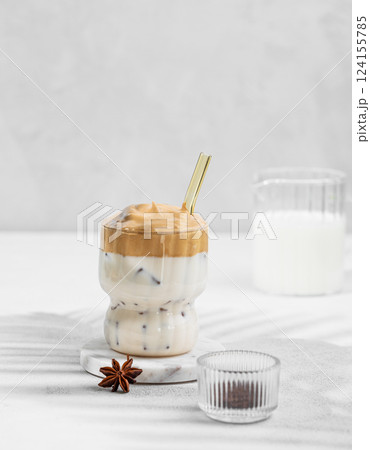 Dalgona coffee in a glass on a light background with milk jug, spices and shadow. 124155785