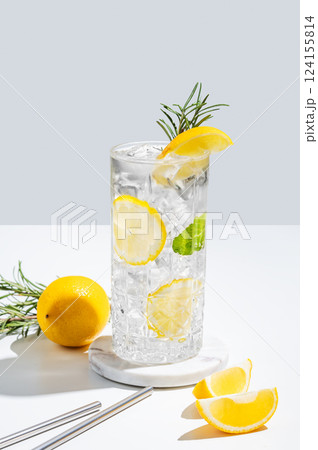 Lemon drink with rosomary and ice in a glass on a light background with shadow and fruits. 124155814