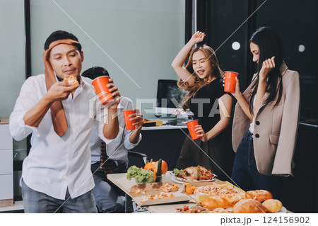 Asian office colleagues and friends enjoy a daytime BBQ with pizza and beer, celebrating Halloween and cheering for their favorite soccer team, creating a lively atmosphere filled with joy. 124156902