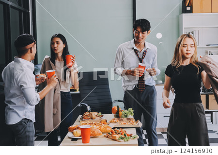 Asian office colleagues and friends enjoy a daytime BBQ with pizza and beer, celebrating Halloween and cheering for their favorite soccer team, creating a lively atmosphere filled with joy. 124156910