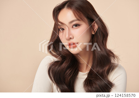 A beautiful young Asian woman with clean, fresh skin against a beige background. Skincare, facial treatment, cosmetology, beauty, and spa. An elegant portrait of an Asian woman. 124158570