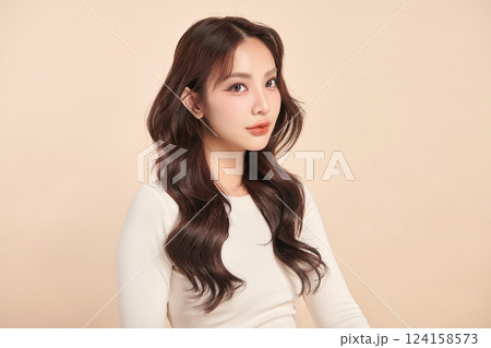 A beautiful young Asian woman with clean, fresh skin against a beige background. Skincare, facial treatment, cosmetology, beauty, and spa. An elegant portrait of an Asian woman. 124158573
