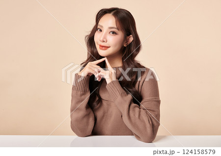 A beautiful young Asian woman with clean, fresh skin against a beige background. Skincare, facial treatment, cosmetology, beauty, and spa. An elegant portrait of an Asian woman. 124158579