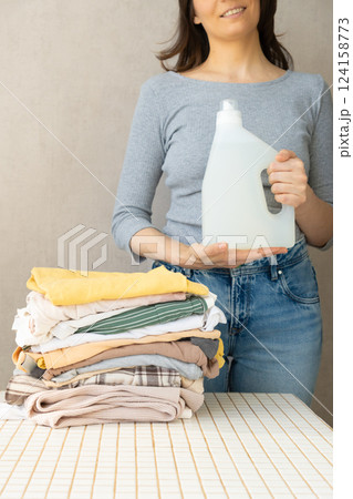 mockup, a happy woman holds a stack of clothes and a laundry gel or conditioner for washing clothes. mockup, a happy woman holds a stack of clothes and a laundry gel or conditioner for washing clothes. 124158773