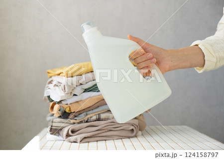 Mockup, woman's hand holding conditioner or laundry gel against a stack of clean clothes. Mockup, woman's hand holding conditioner or laundry gel against a stack of clean clothes. 124158797