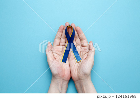 A person holds a yellow and blue awareness ribbon, symbolizing World Down Syndrome Day A person holds a yellow and blue awareness ribbon, symbolizing World Down Syndrome Day 124161969