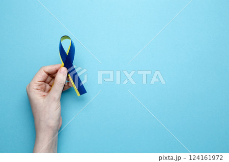 A person holds a yellow and blue awareness ribbon, symbolizing World Down Syndrome Day A person holds a yellow and blue awareness ribbon, symbolizing World Down Syndrome Day 124161972