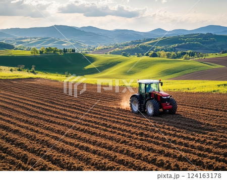 Satellite-guided tractor plowing straight furrows in a fertile field, surrounded by rolling hills 124163178