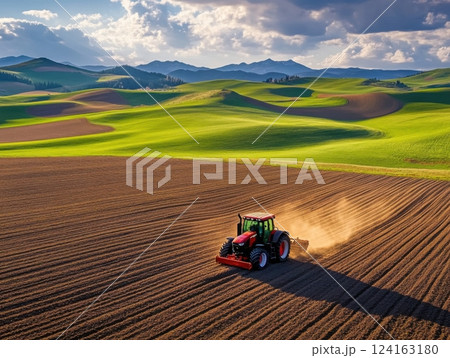 Satellite-guided tractor plowing straight furrows in a fertile field, surrounded by rolling hills 124163180