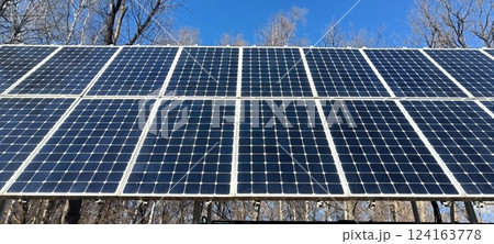 In a forested location, solar panels stand tall against a clear blue sky, capturing sunlight for energy production. The scene highlights clean technology and environmental sustainability In a forested location, solar panels stand tall against a clear blue sky, capturing sunlight for energy production. The scene highlights clean technology and environmental sustainability 124163778