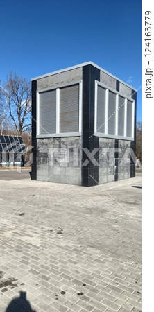 A contemporary building with sleek lines and grey exterior features large vents and is set in an open urban park. Solar panels are visible nearby under bright sunlight 124163779