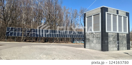A solar panel array extends alongside a contemporary structure in a forested location. The installation captures sunlight efficiently while blending with nature 124163780