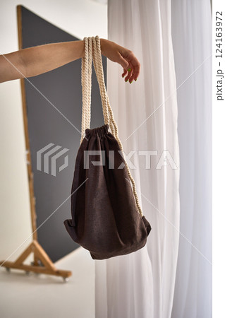 Hand Holding Stylish Drawstring Bag with Rope Handles, Minimalist Fashion Accessory in Studio Light Concept Hand Holding Stylish Drawstring Bag with Rope Handles, Minimalist Fashion Accessory in Studio Light Concept 124163972