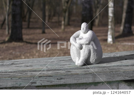 A plaster statue of a full-figured, dreamy woman on a wooden bench in a spring park 124164057