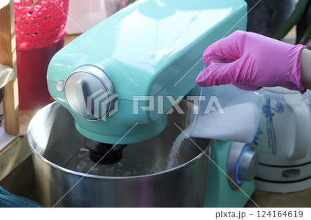 A woman adds sugar to the bowl of a planetary mixer. Preparing marshmallow mixture. Close-up. A woman adds sugar to the bowl of a planetary mixer. Preparing marshmallow mixture. Close-up. 124164619
