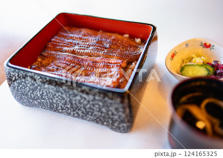 Hot-smoked eel with a caramelized soy glaze served atop white rice in traditional lacquered box 124165325