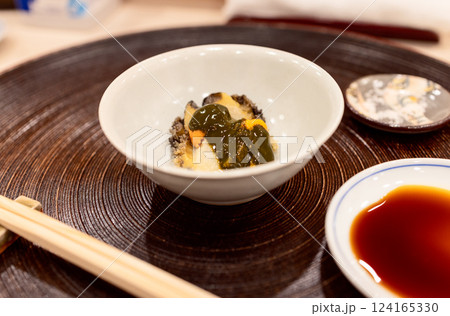 Abalone sashimi topped with sea urchin, elegantly served in a ceramic bowl with soy sauce on side 124165330