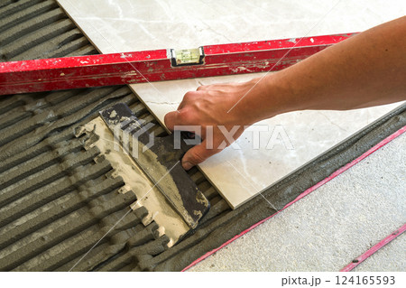 Ceramic tiles and tools for tiler. Worker hand installing floor tiles. Home improvement, renovation - ceramic tile floor adhesive, mortar, level. 124165593