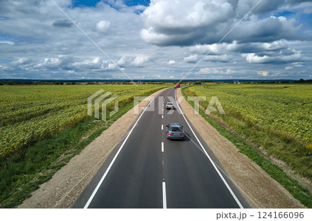 Aerial view of intercity road between green agricultural fields with fast driving cars. Top view from drone of highway traffic Aerial view of intercity road between green agricultural fields with fast driving cars. Top view from drone of highway traffic 124166096